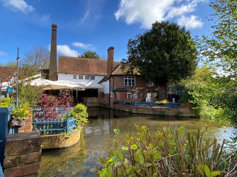 The Waffle House at Kingsbury Watermill in St Albans, with the old mill building reflected in the water and spring greenery framing the scene.